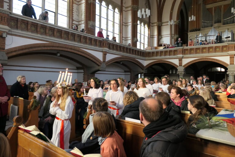 Lucia im weißen Gewand und mit Kerzen auf dem Kopf läuft in der Kirche entlang